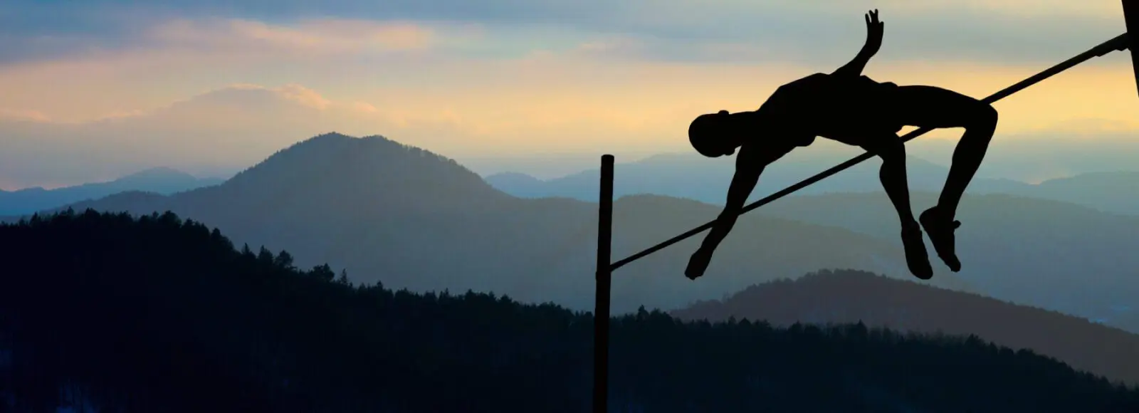 Silhouette of athlete jumping pole vault with mountains in the background